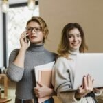 <font dir="auto" style="vertical-align: inherit;"><font dir="auto" style="vertical-align: inherit;">Prendre soin de soi pour prendre soin des autres</font></font> Two women collaborate in a modern office environment, balancing work with technology.
