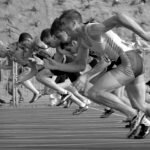 <font dir="auto" style="vertical-align: inherit;"><font dir="auto" style="vertical-align: inherit;">Prendre soin de soi pour prendre soin des autres</font></font> Athletes burst from the blocks during a sprint race, captured in monochrome.